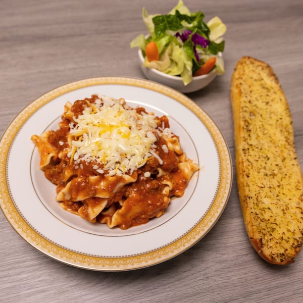 Pasta with meat sauce and melted cheese, served with a side salad and garlic bread.