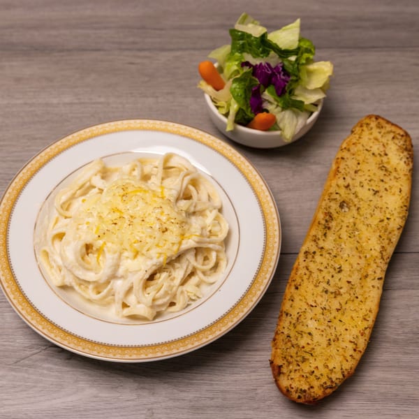 Creamy fettuccine alfredo with grated cheese, a side salad, and a large piece of garlic bread.