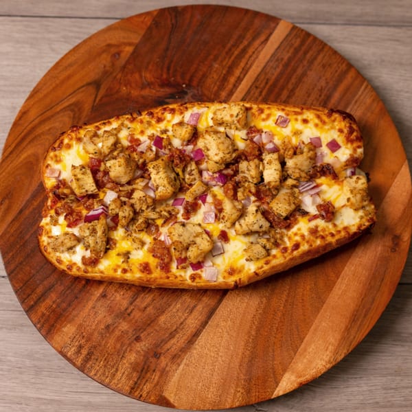 Can Am Pizza's chicken and bacon pizza bread, topped with red onions, on a wooden board.