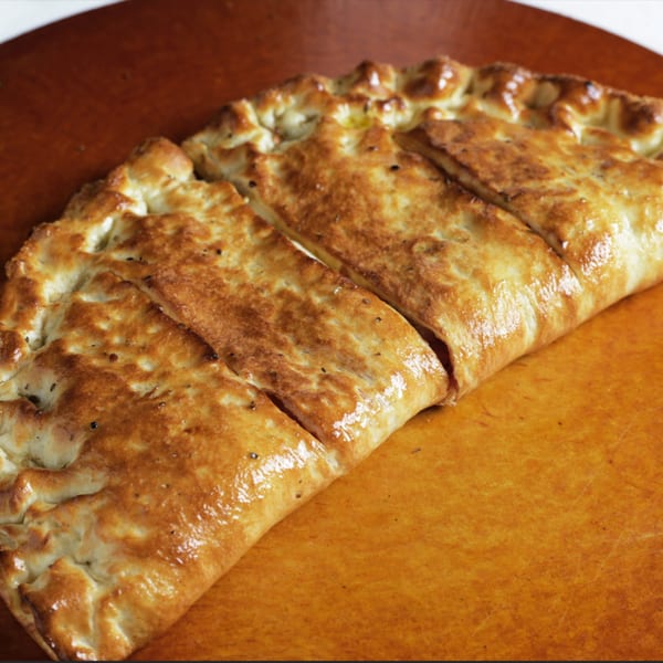 A golden-brown, baked calzone from Can Am Pizza, sliced into three portions on a wooden surface.