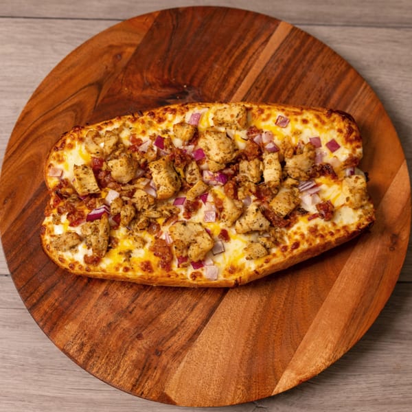 Can Am Pizza's cheesy bread with chicken, bacon, and red onions on a wooden board.