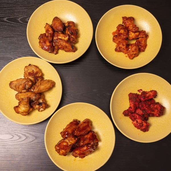 Five yellow plates of Can Am Pizza chicken wings, each with a different sauce, on a dark table.
