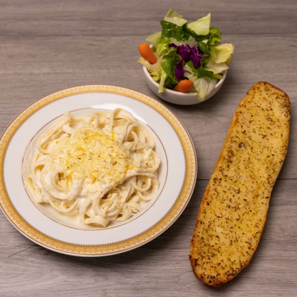Fettuccine Alfredo pasta with grated cheese, a side salad, and a piece of garlic bread.