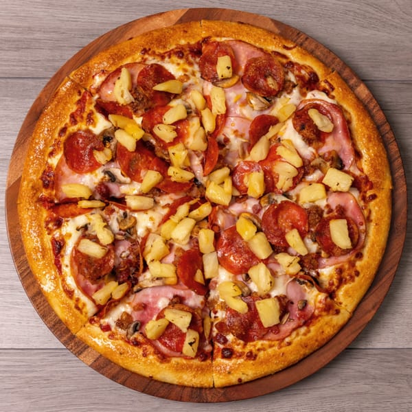 A Can Am Pizza with pepperoni, ham, mushrooms, and pineapple on a wooden serving board.